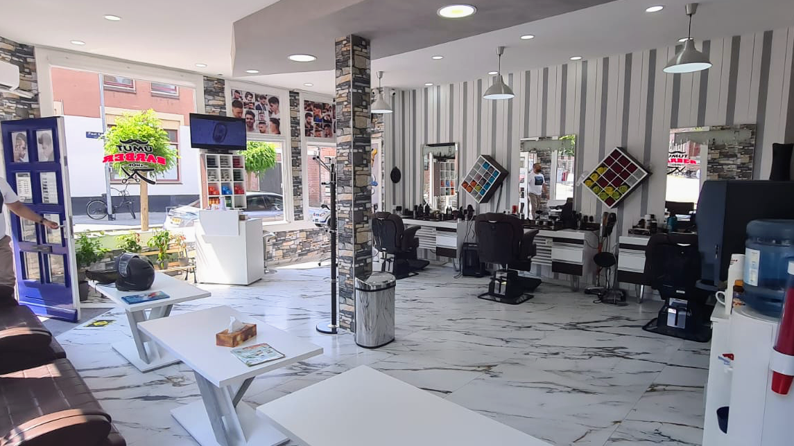 Het interieur van Umut Barbershop: witte marmeren vloer, kappersstoelen voor de spiegels en grijs gestreept behang